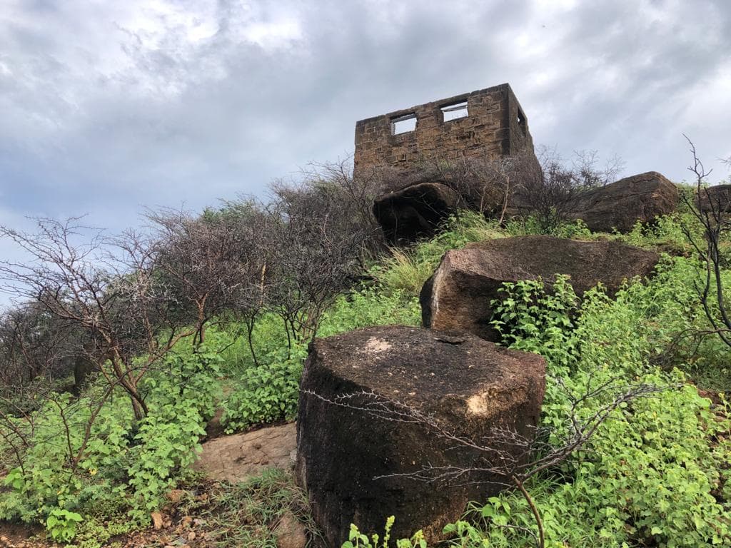 Ruined stone building perched on a rocky hill with green vegetation